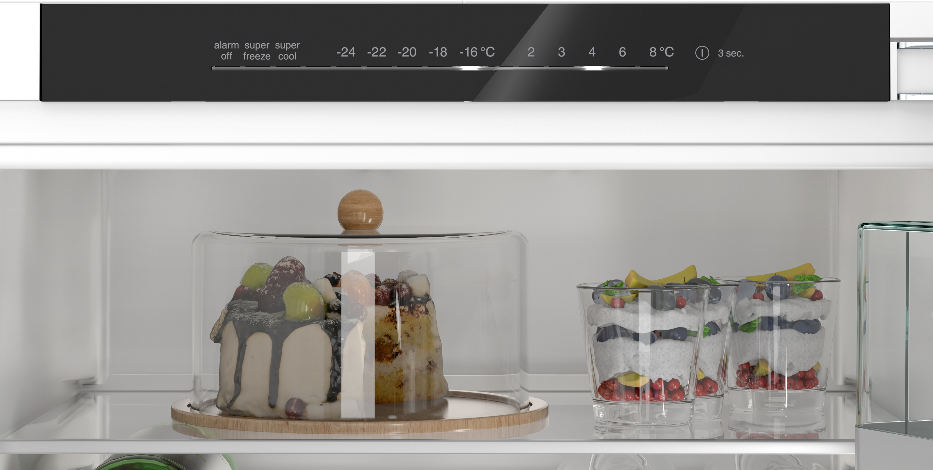 Ein Kuchen unter einer Glasglocke und zwei Dessertgläser mit Früchten in einem Kühlschrank.