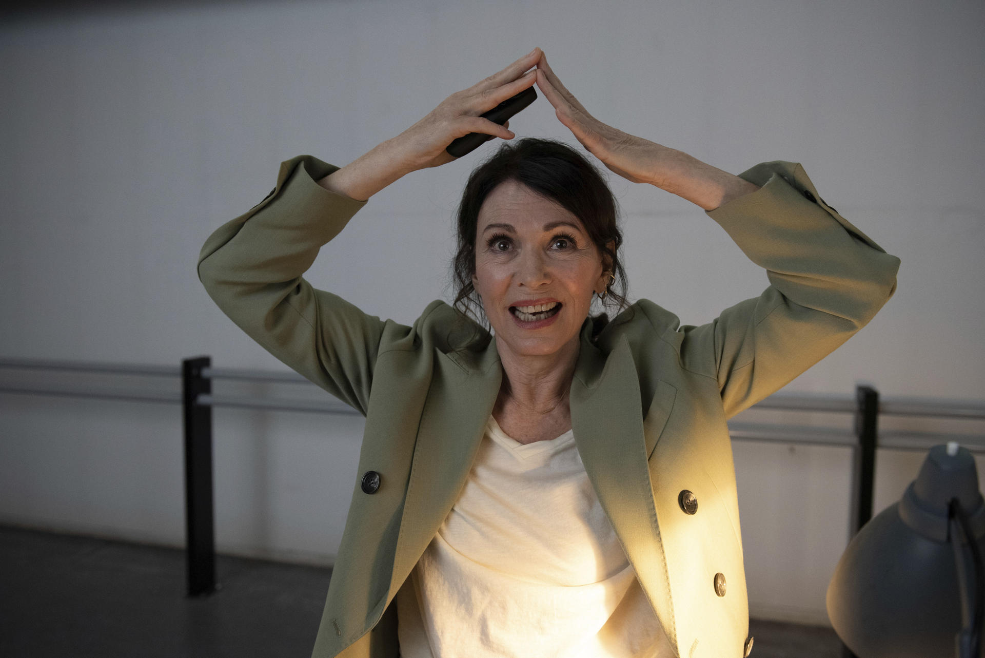 Eine Frau mit dunklem Haar hält ein Handy über ihrem Kopf, trägt eine grüne Jacke.
