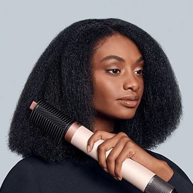 Kobieta z ciemnymi włosami używa różowo-czarnej szczotki do suszenia włosów.