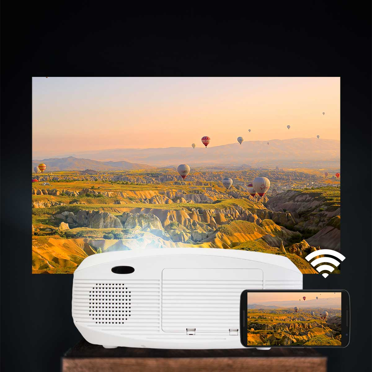 Un proyector blanco muestra un paisaje con globos aerostáticos. Un smartphone refleja la imagen.