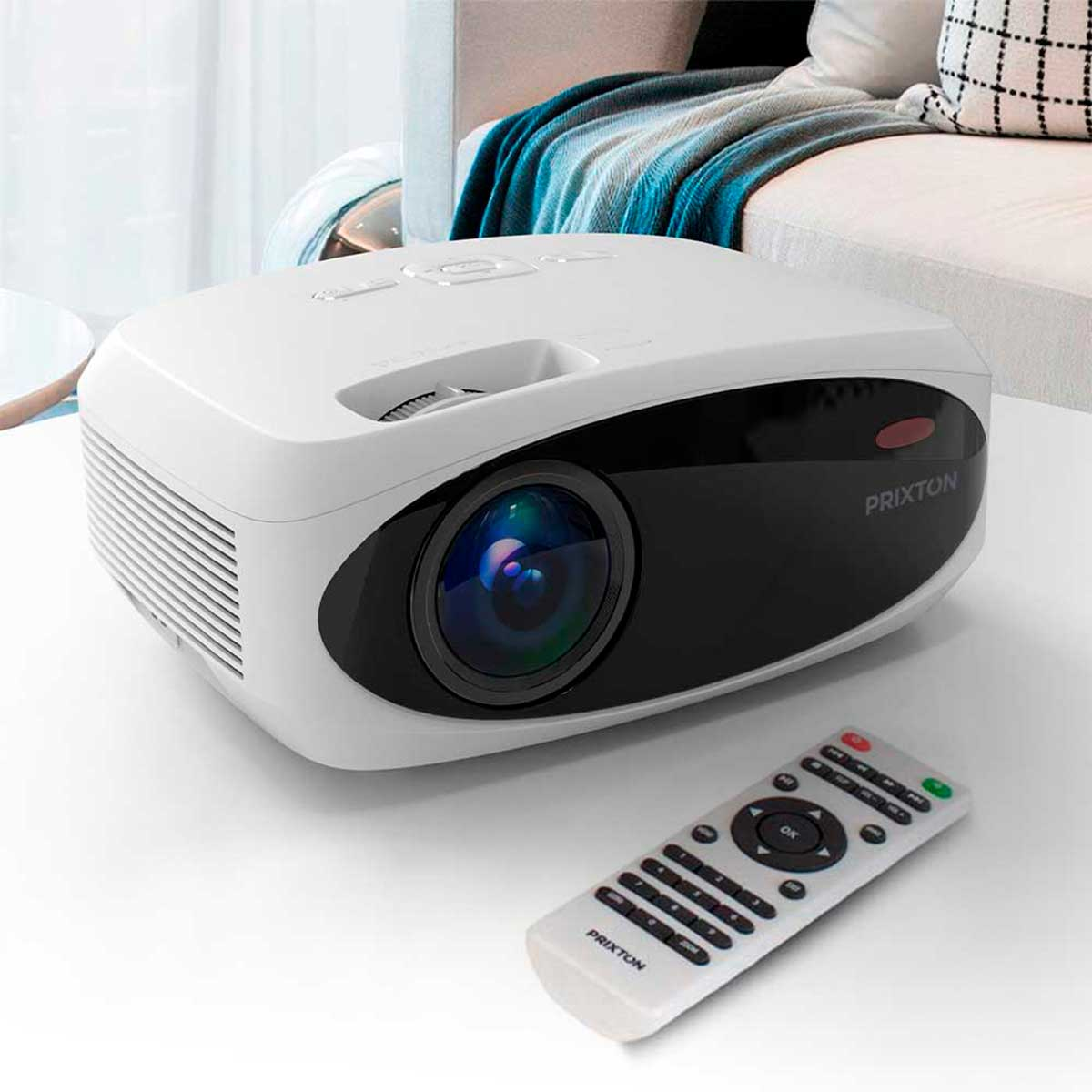 Un proyector blanco con mando a distancia sobre una mesa. Un sofá al fondo.