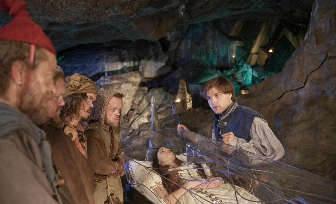 Zwerge betrachten eine schlafende Frau in einem Glaskasten in einer Höhle.