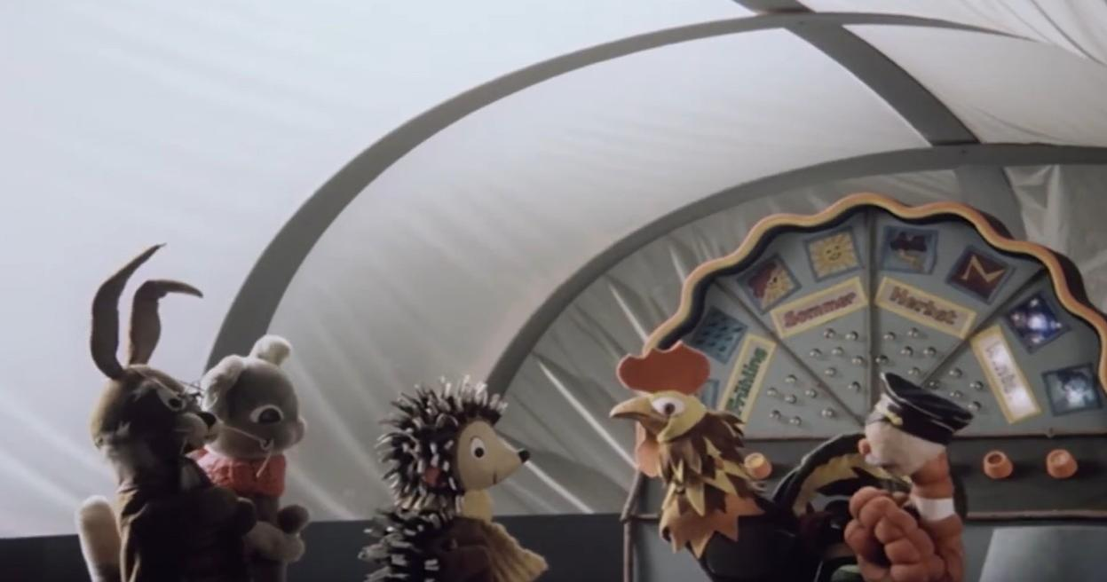 Puppen von Hasen, einem Igel und einem Hahn stehen vor einem Rad mit Jahreszeiten.
