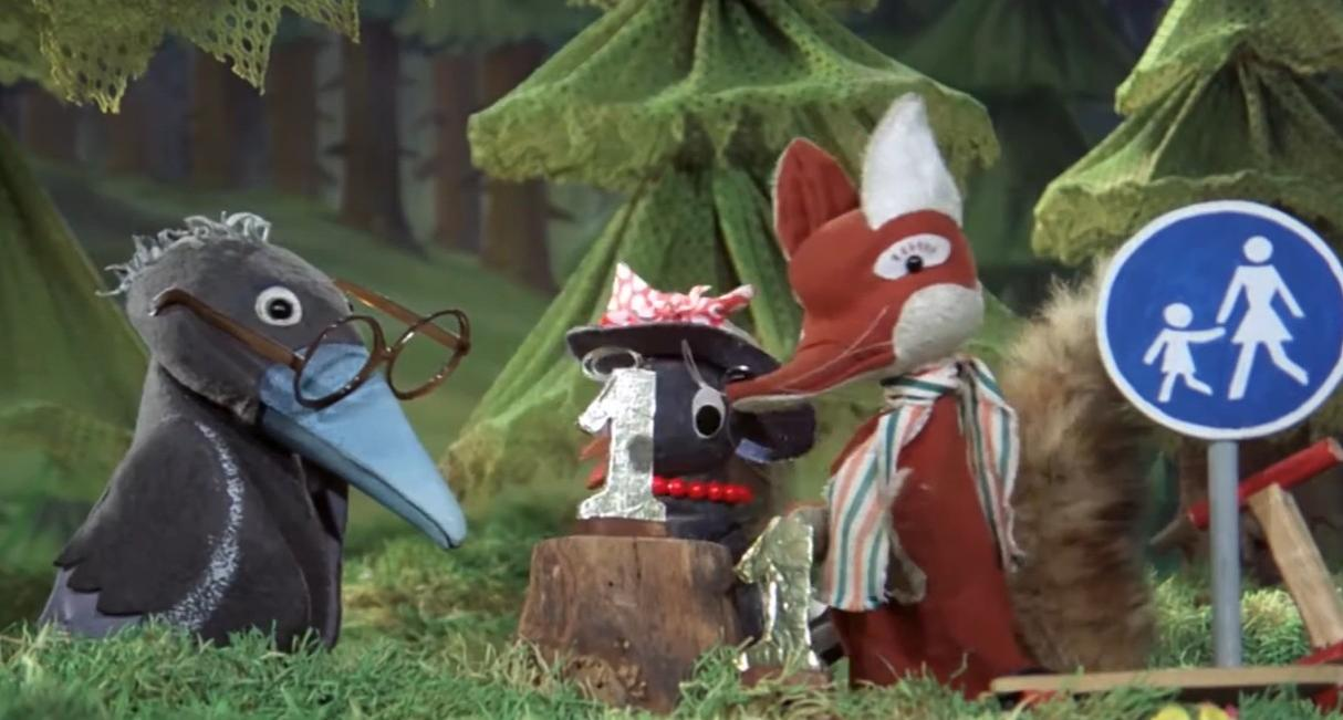 Ein Vogel mit Brille, eine Maus mit Hut und ein Fuchs stehen im Wald neben einem Schild.
