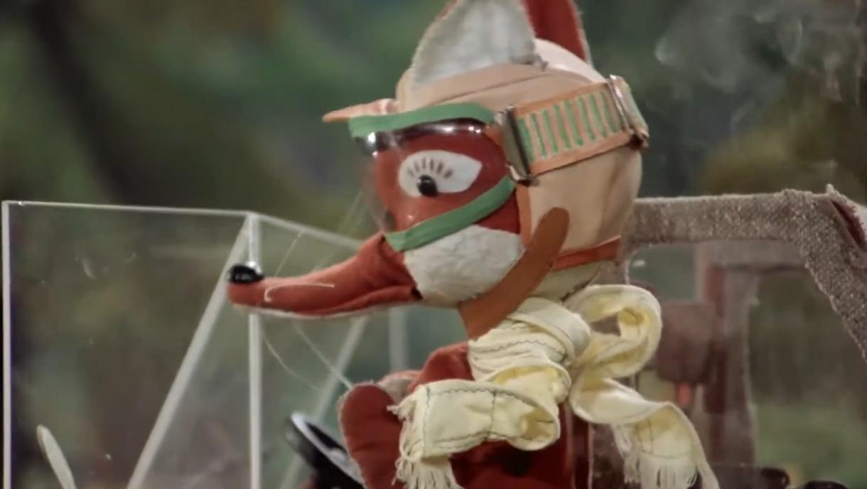 Ein Fuchs-Plüschtier mit Pilotenmütze und Schal sitzt im Auto.