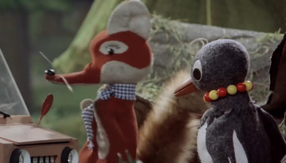 Ein Fuchs und ein Vogel sitzen neben einem Auto im Wald.