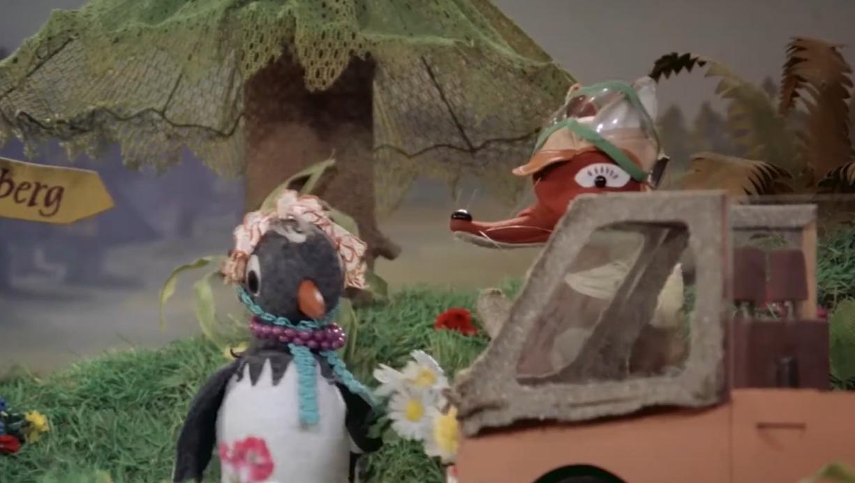 Ein Pinguin mit Blumen steht neben einem Auto, ein Fuchs schaut aus dem Fenster.