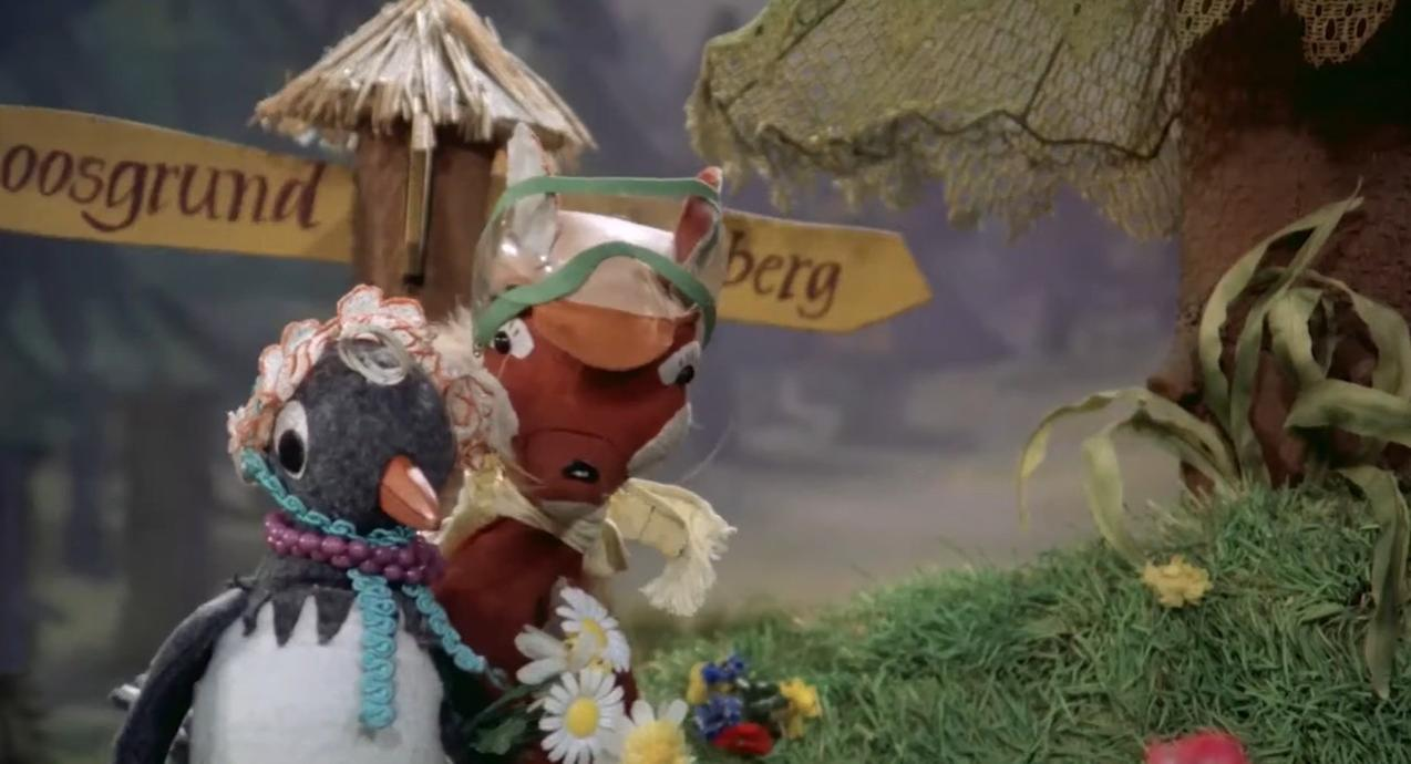 Ein Pinguin und ein Pferd stehen vor Wegweisern im Wald.