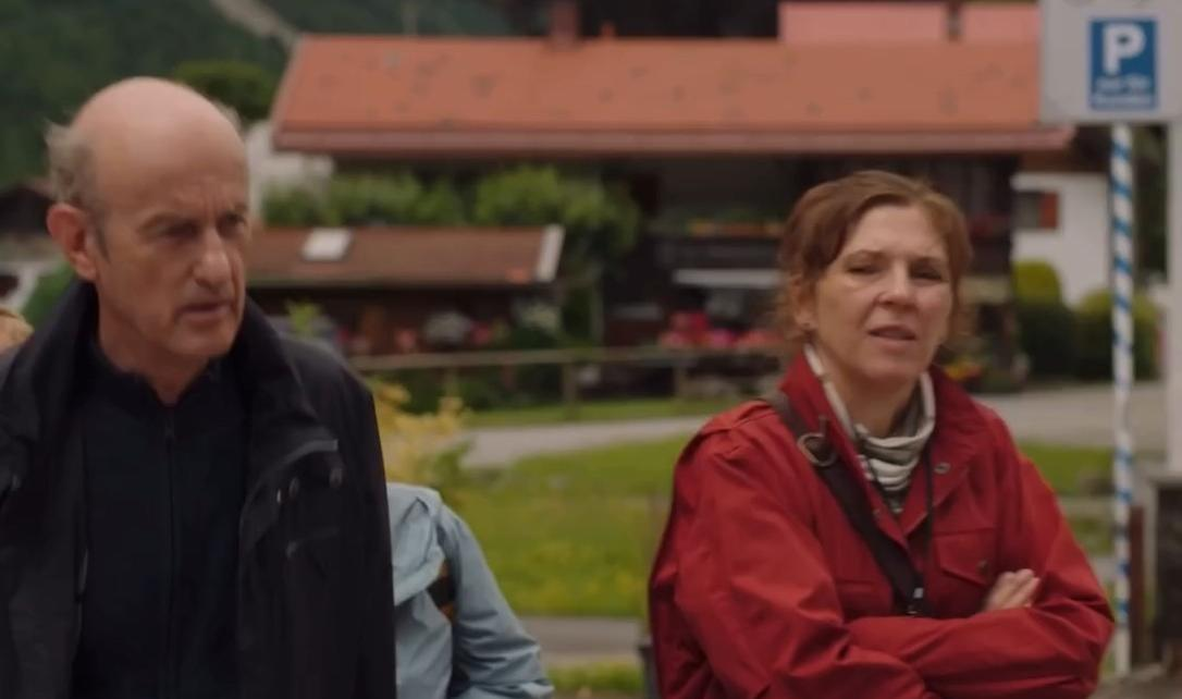 Mann und Frau stehen vor Häusern. Ein Parkschild ist sichtbar.