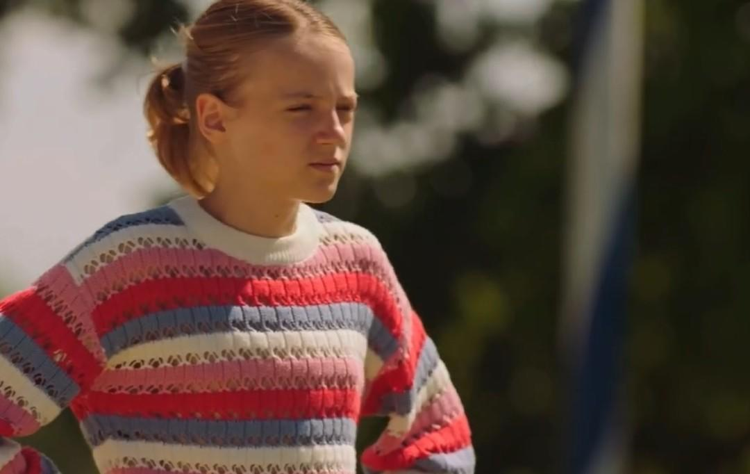Ein junges Mädchen mit Pferdeschwanz trägt einen gestreiften Pullover. Draußen.