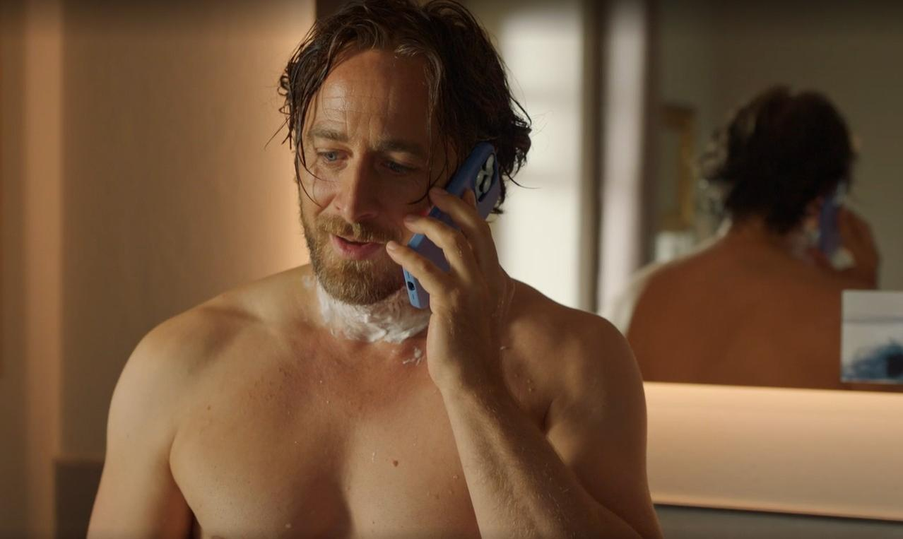 Ein Mann mit Rasierschaum im Gesicht telefoniert mit einem blauen Handy.