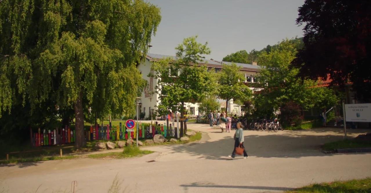 Eine Schule mit Bäumen und Fahrrädern. Menschen gehen auf dem Gelände.