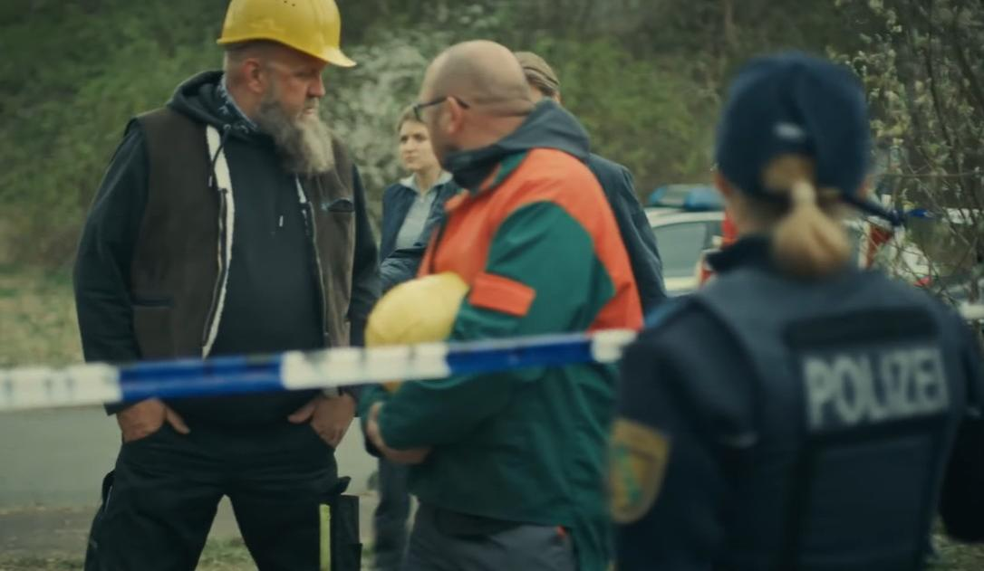 Polizisten und Bauarbeiter stehen hinter Flatterband. Einer hält einen gelben Helm.