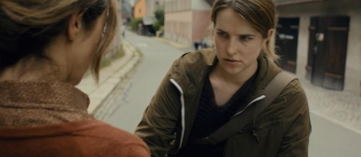 Zwei Frauen sprechen sich auf einer Straße mit Häusern im Hintergrund an.