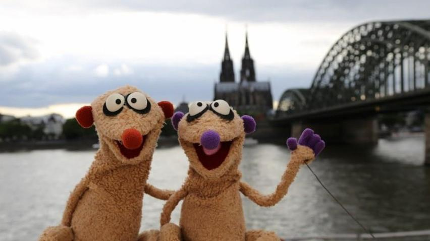 Zwei Puppen stehen vor einer Brücke und Kathedrale am Flussufer.
