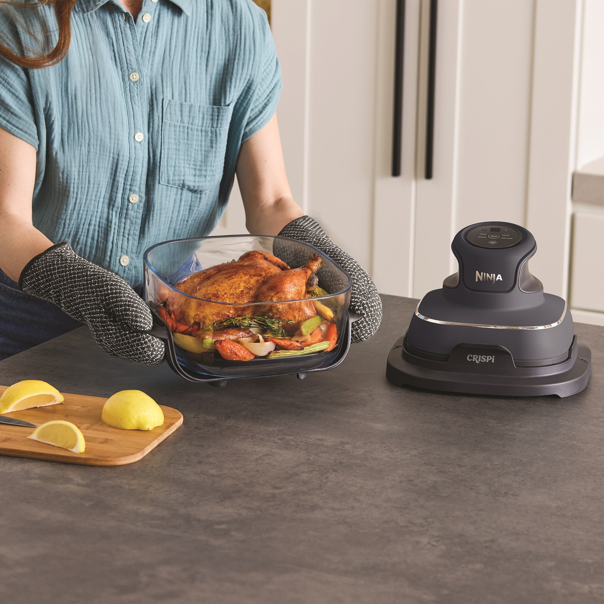 Osoba w rękawicach kuchennych wyjmuje pieczonego kurczaka ze szklanej formy z warzywami.