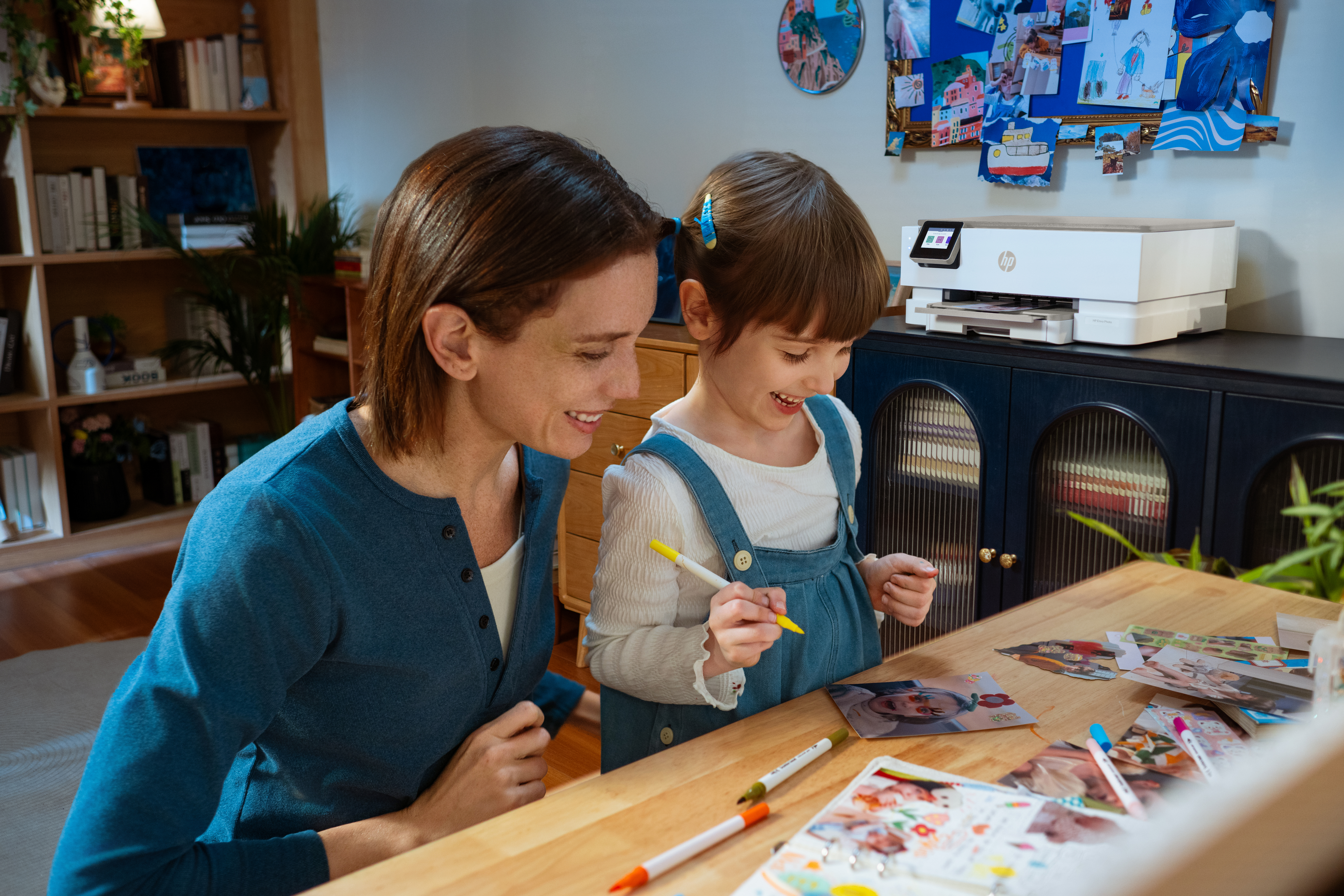 Donna e bambina creano con foto e pennarelli su tavolo legno.