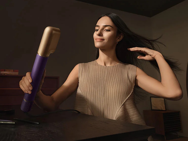 Kobieta z ciemnymi włosami trzyma fioletowo-złotą suszarkę.