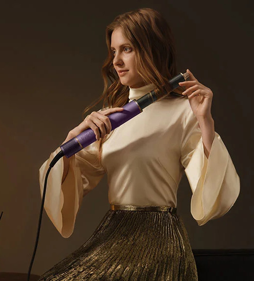 Kobieta z długimi brązowymi włosami używa fioletowej lokówki do włosów.