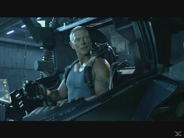 Ein Mann mit grauem Haar sitzt in einem Cockpit und trägt ein blaues Tanktop.