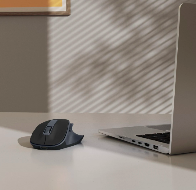 Czarna mysz komputerowa obok laptopa na biurku. Wzór cienia na ścianie.