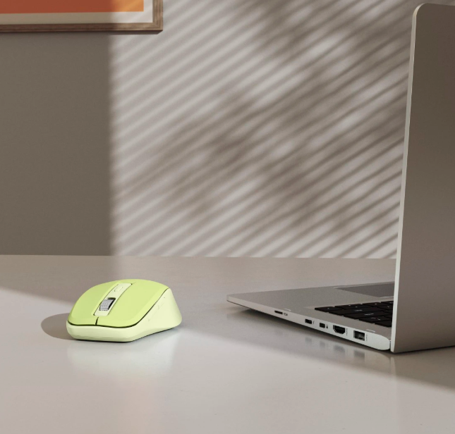 Żółta myszka na biurku obok otwartego laptopa. Światło rzuca cienie.