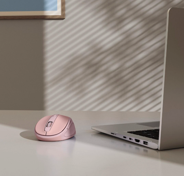 Różowa mysz komputerowa leży na białym biurku obok laptopa.