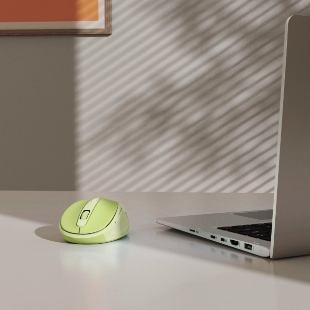 Zielona mysz komputerowa obok laptopa na białym biurku.