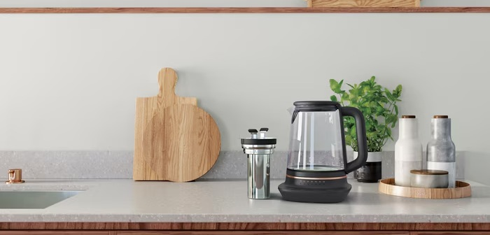 Blat kuchenny z drewnianą deską, czajnikiem, rośliną i butelkami.