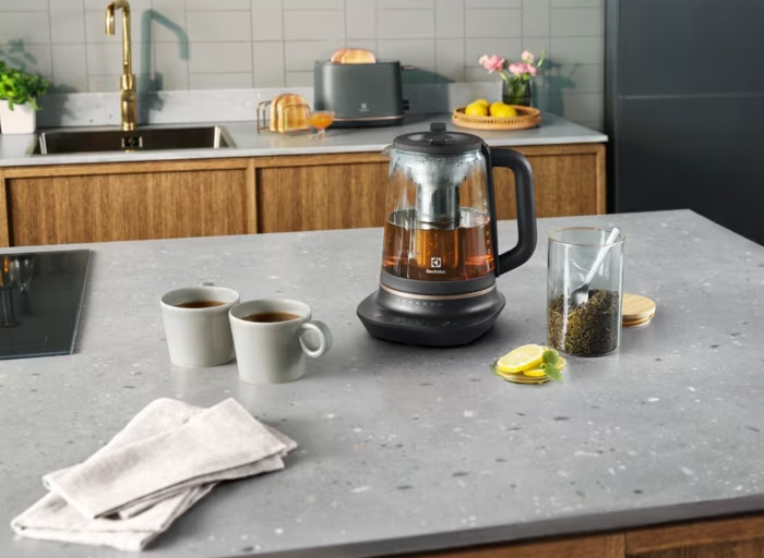 Czajnik z dwoma filiżankami herbaty, plasterkami cytryny i liśćmi herbaty na blacie kuchennym.