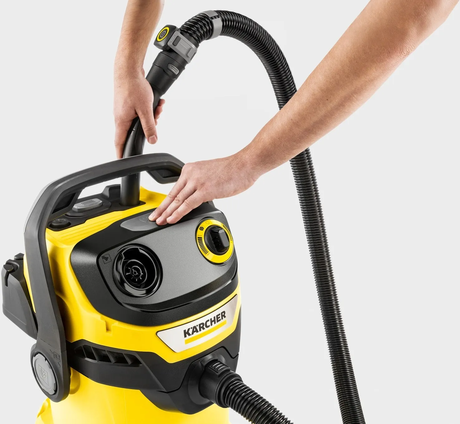 Żółty odkurzacz Kärcher z czarnym wężem trzymany przez ręce.