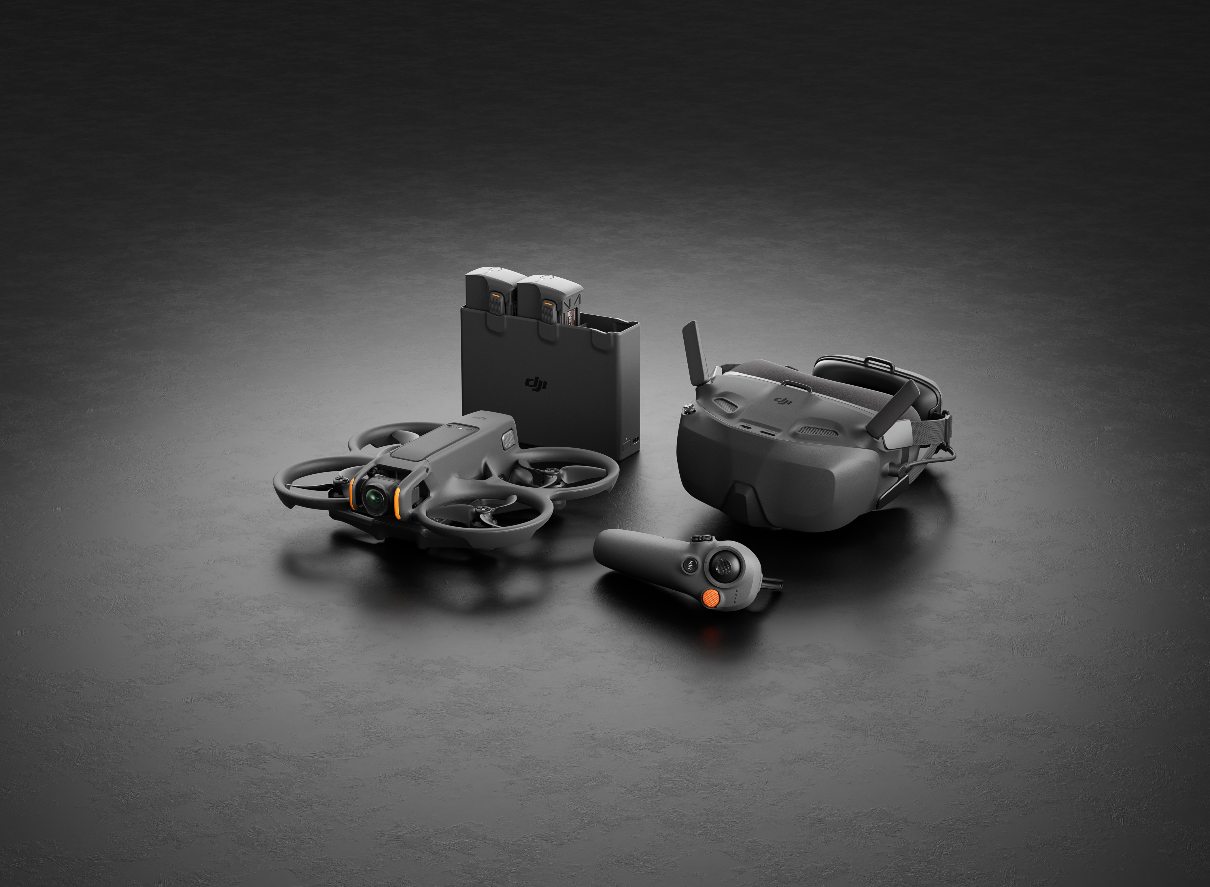 Gri DJI drone, gözlük, kumanda ve piller karanlık yüzeyde.