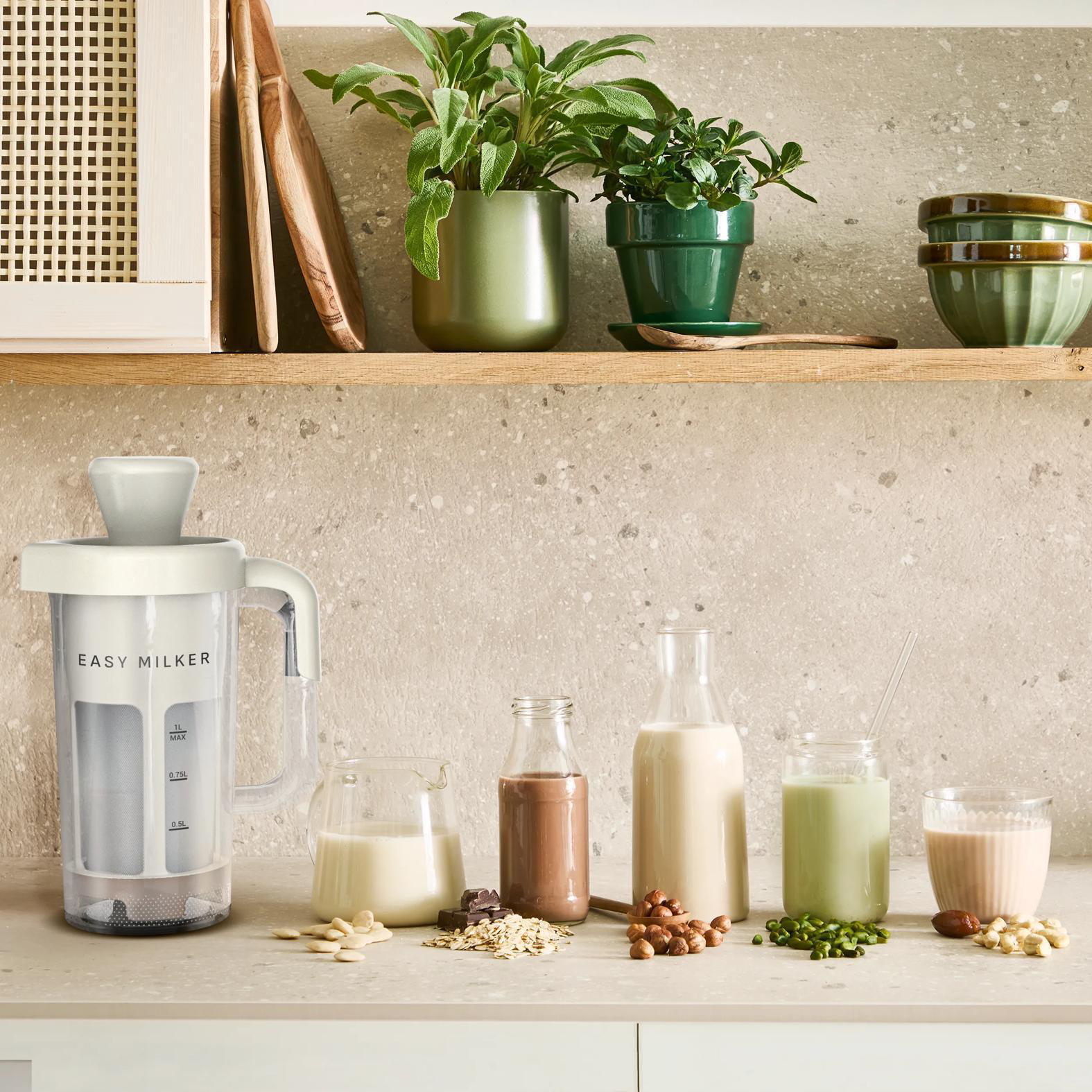 Eine weiße Milchmaschine steht neben Flaschen mit Milch, Schokolade und grünen Getränken.