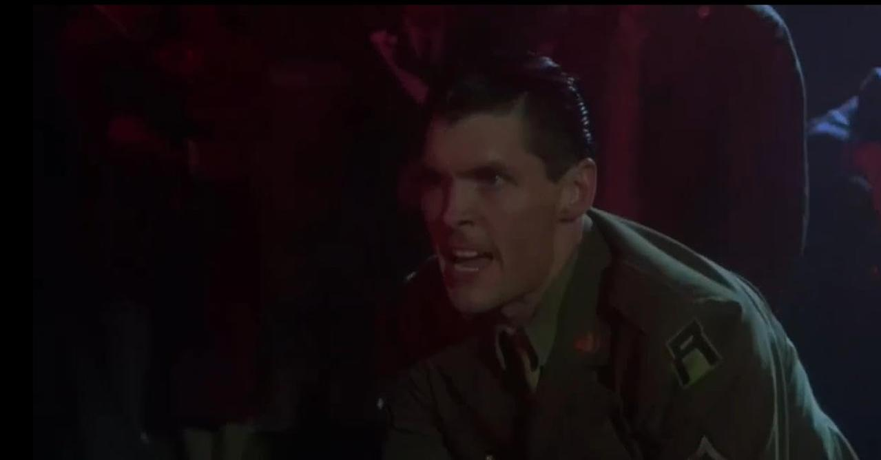 Ein Mann in Militäruniform mit einem ernsten Gesichtsausdruck, im Dunkeln.