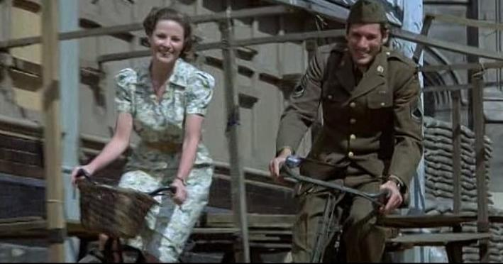 Ein Mann in Uniform und eine Frau auf Fahrrädern fahren nebeneinander. Sie lächeln.