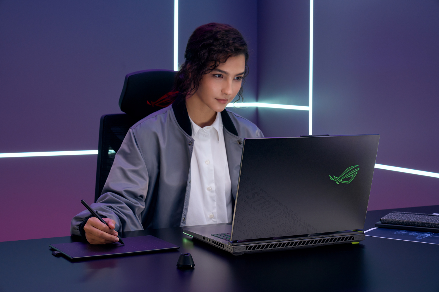 Een vrouw met donker krullend haar zit aan een bureau met een laptop en tekentablet.