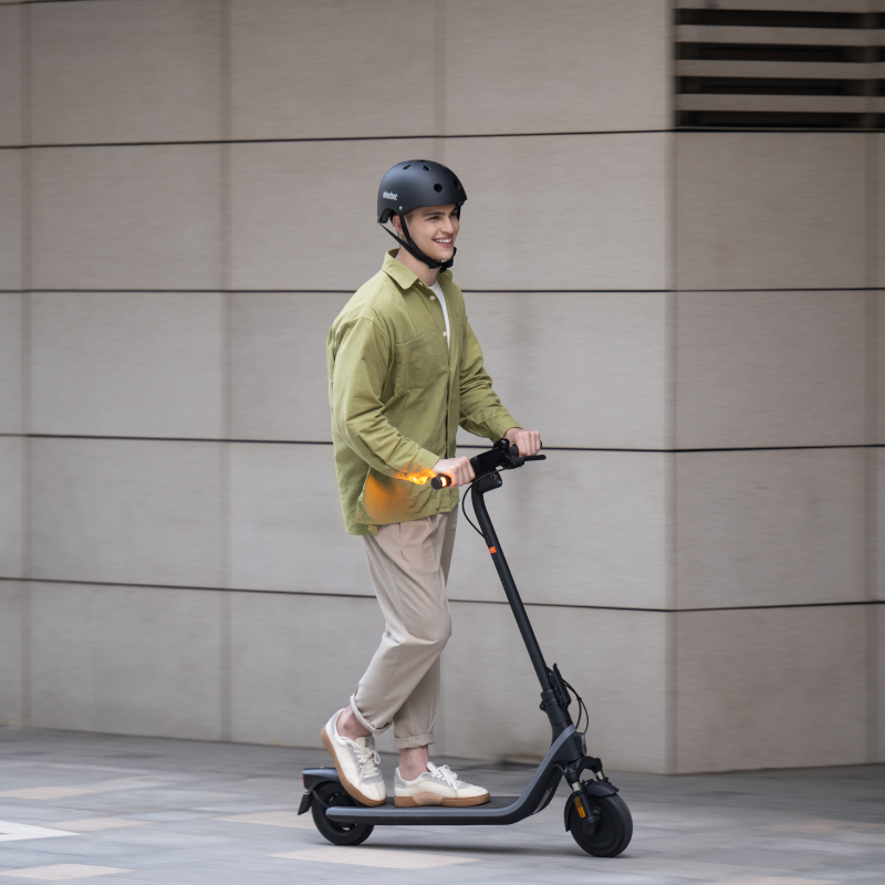 Kasklı adam, haki gömlek ve pantolon giymiş, elektrikli scooter sürüyor.