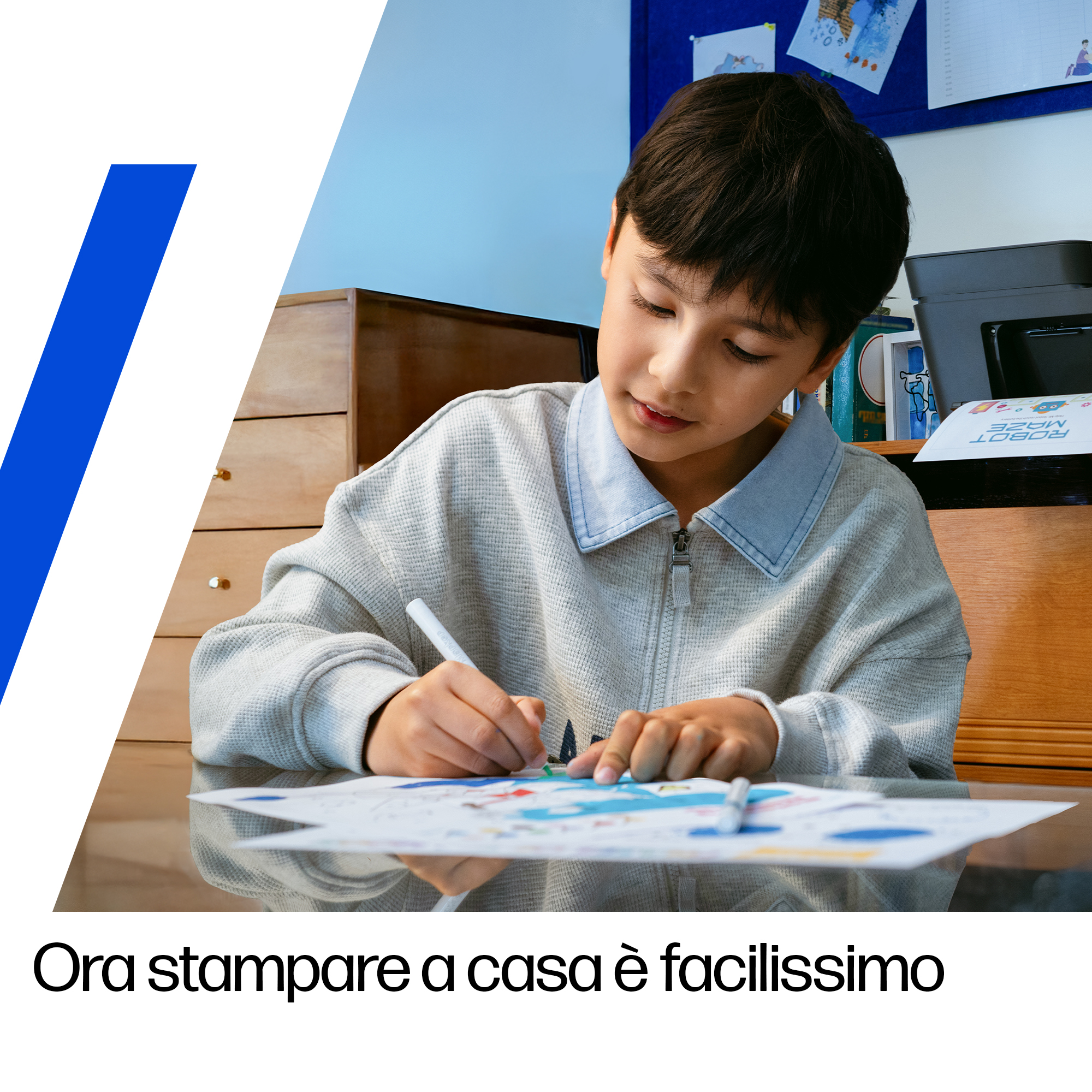 Un ragazzo seduto a un tavolo, disegna con una penna su un foglio di carta.