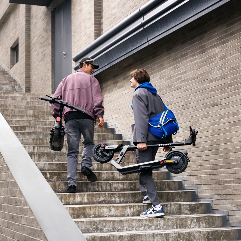 İki kişi beton merdivenlerden elektrikli scooter taşıyor.