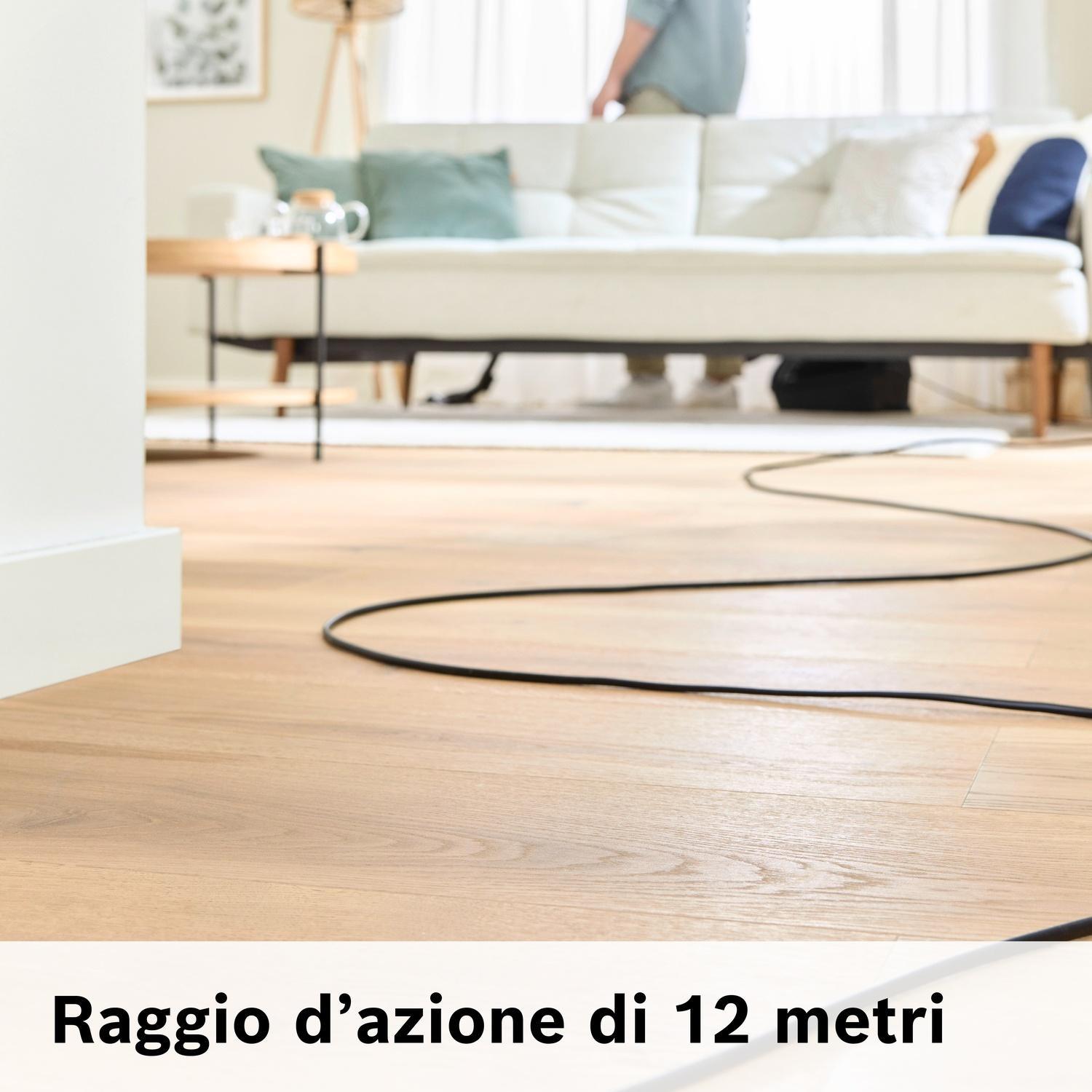 Un cavo nero su un pavimento in legno in un soggiorno con divano bianco.