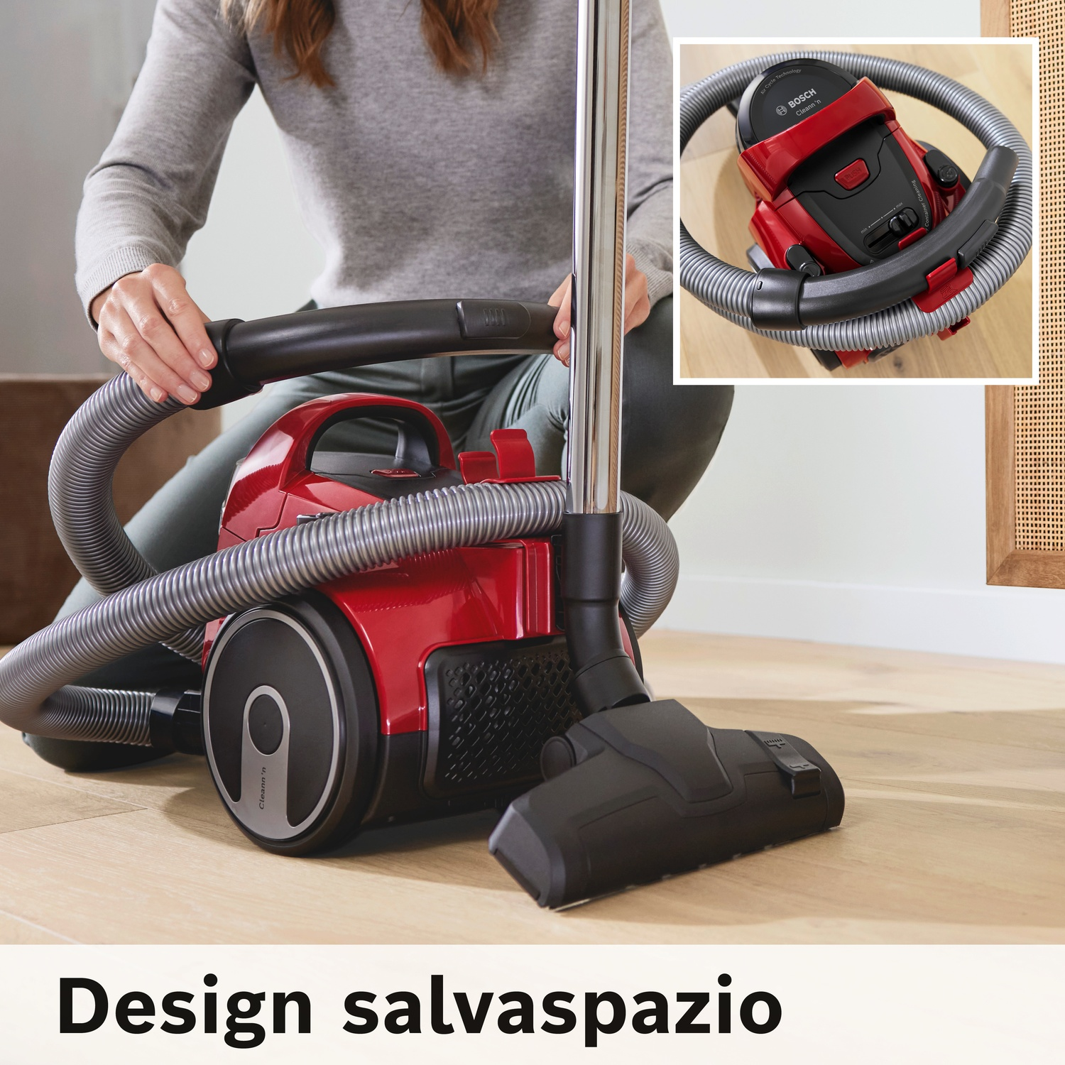 Una persona in ginocchio tiene la maniglia di un aspirapolvere Bosch rosso. Primo piano.