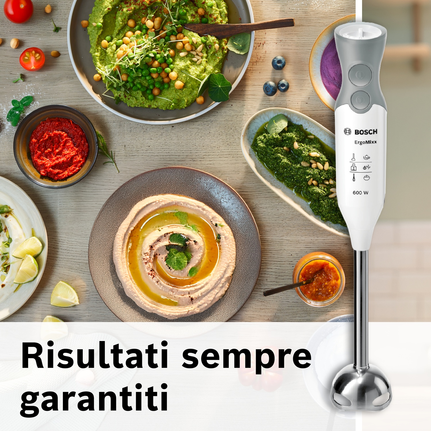Un frullatore a immersione Bosch accanto a ciotole di hummus, pesto e salsa.