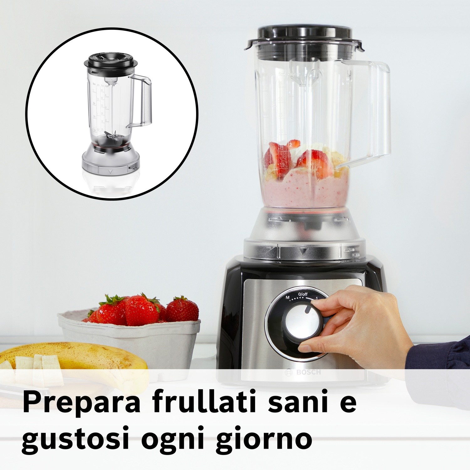 Una mano gira la manopola di un frullatore con fragole e banane.