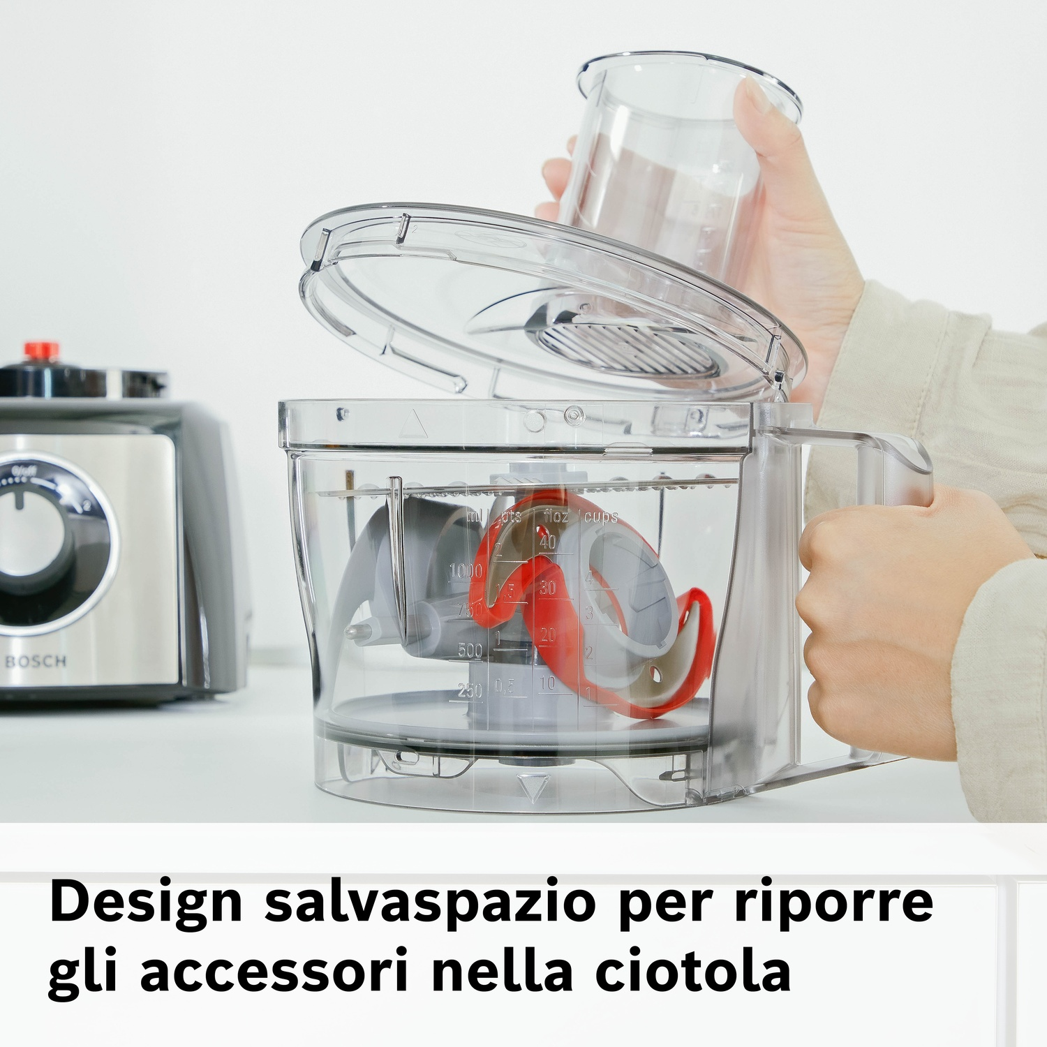 Una mano inserisce un misurino in un robot da cucina con lame rosse.