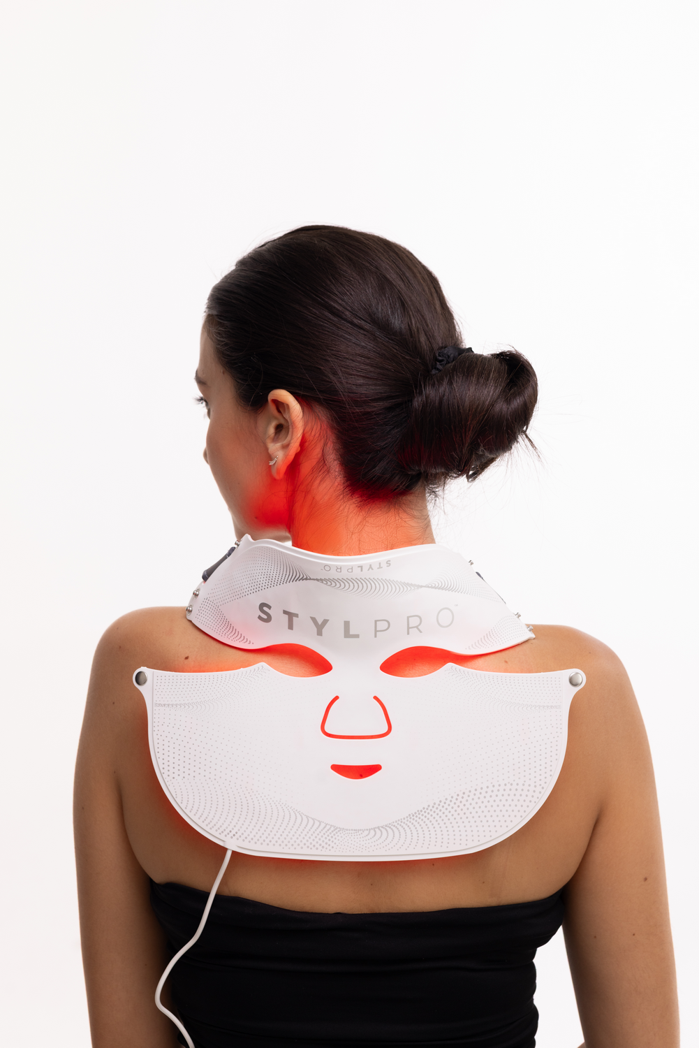 Una mujer con el pelo recogido lleva una mascarilla facial blanca con luz roja.