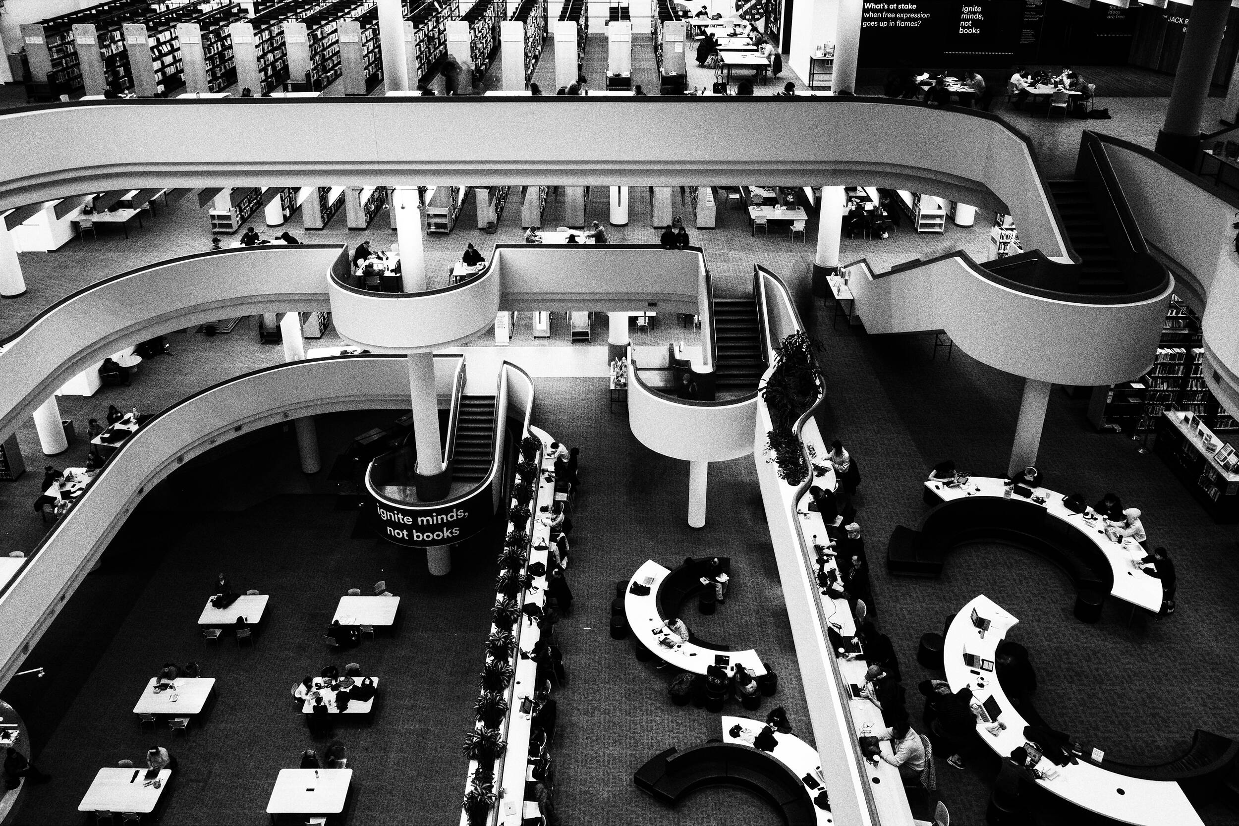 Intérieur d'une bibliothèque à plusieurs niveaux avec des gens étudiant à des tables et des bureaux. Des étagères bordent les murs.