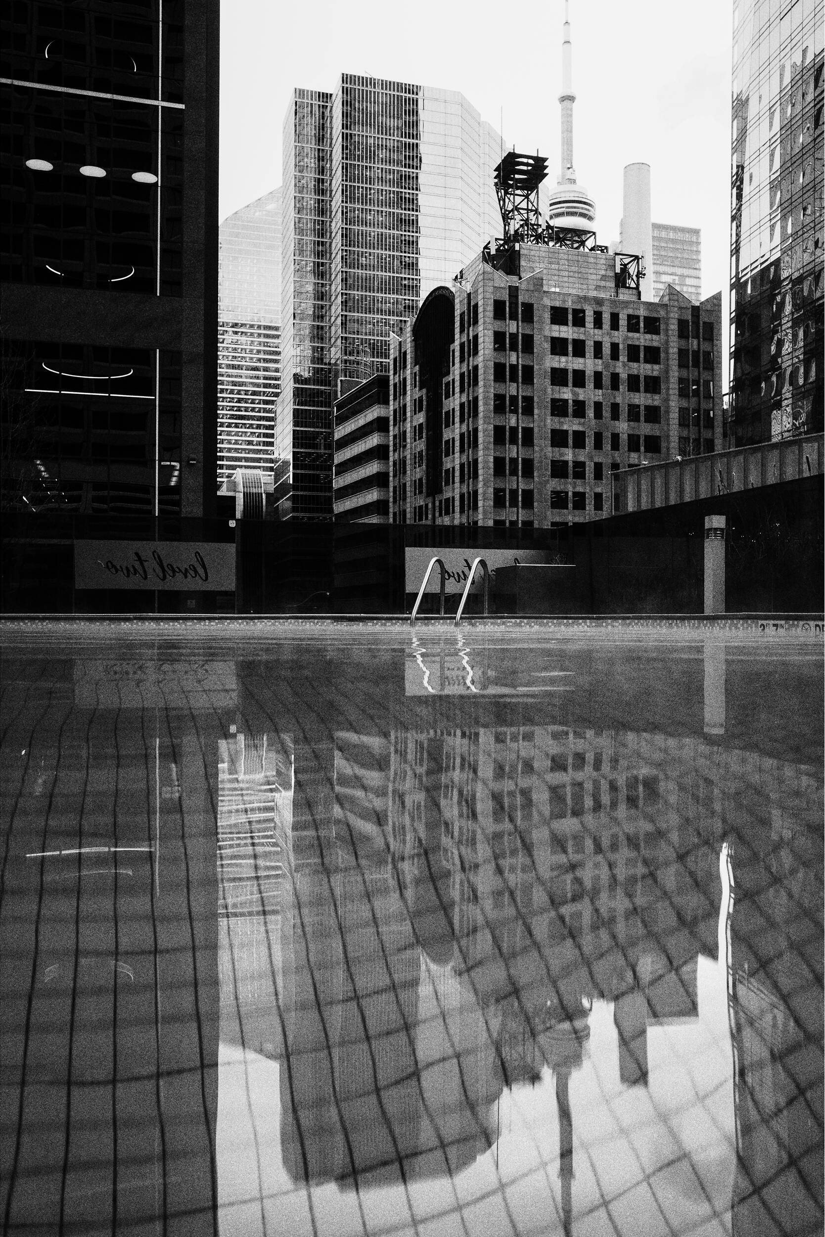 Une piscine reflète des gratte-ciel et une tour en noir et blanc.