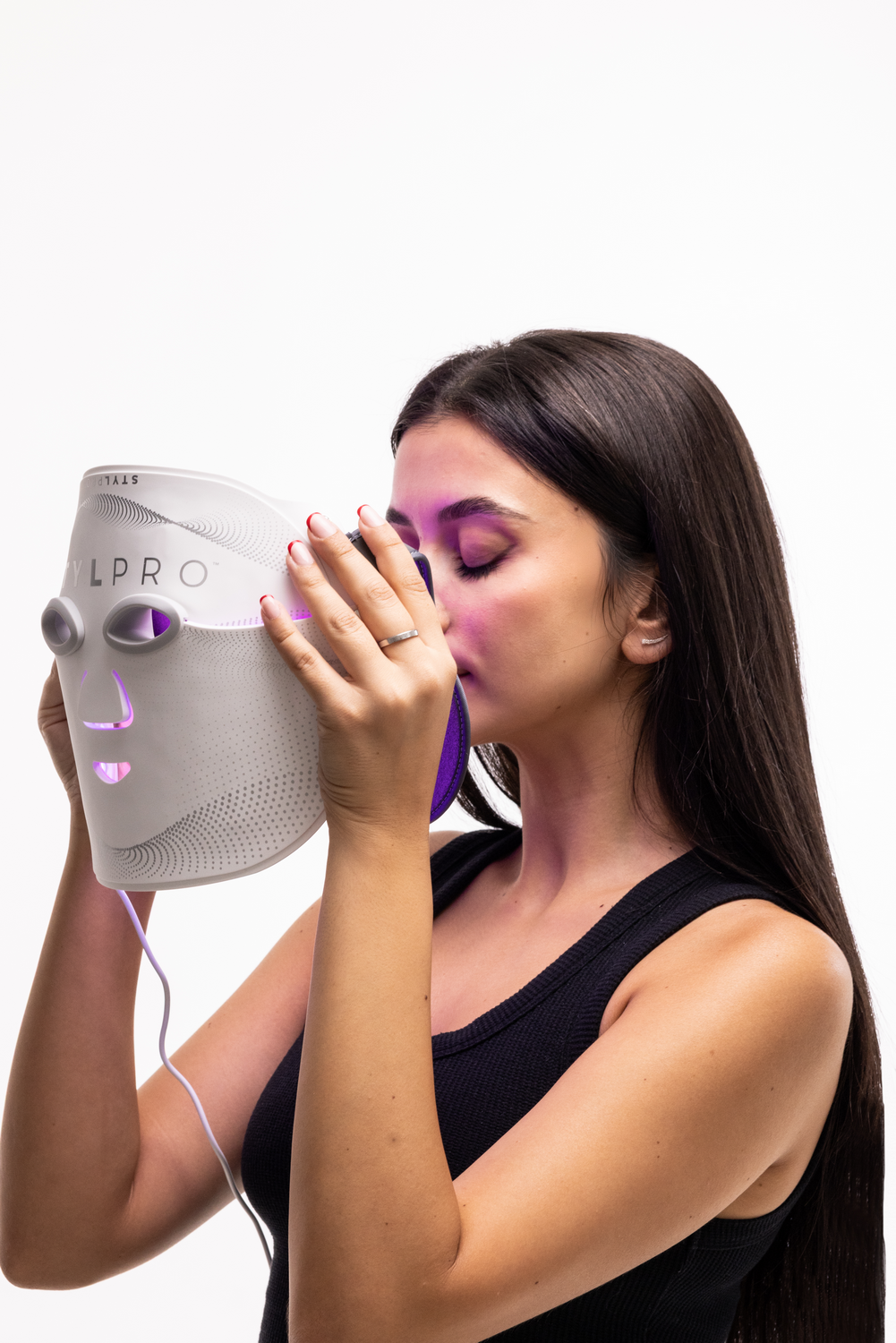 Una mujer con cabello largo y oscuro sostiene una mascarilla facial LED blanca.