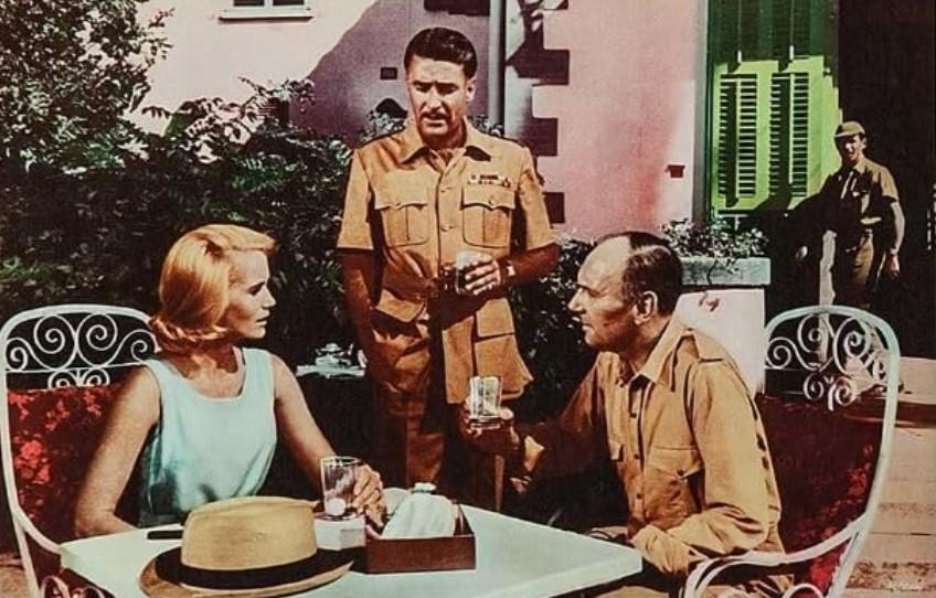 Drei Personen in Khaki-Kleidung sitzen und stehen draußen an einem Tisch.