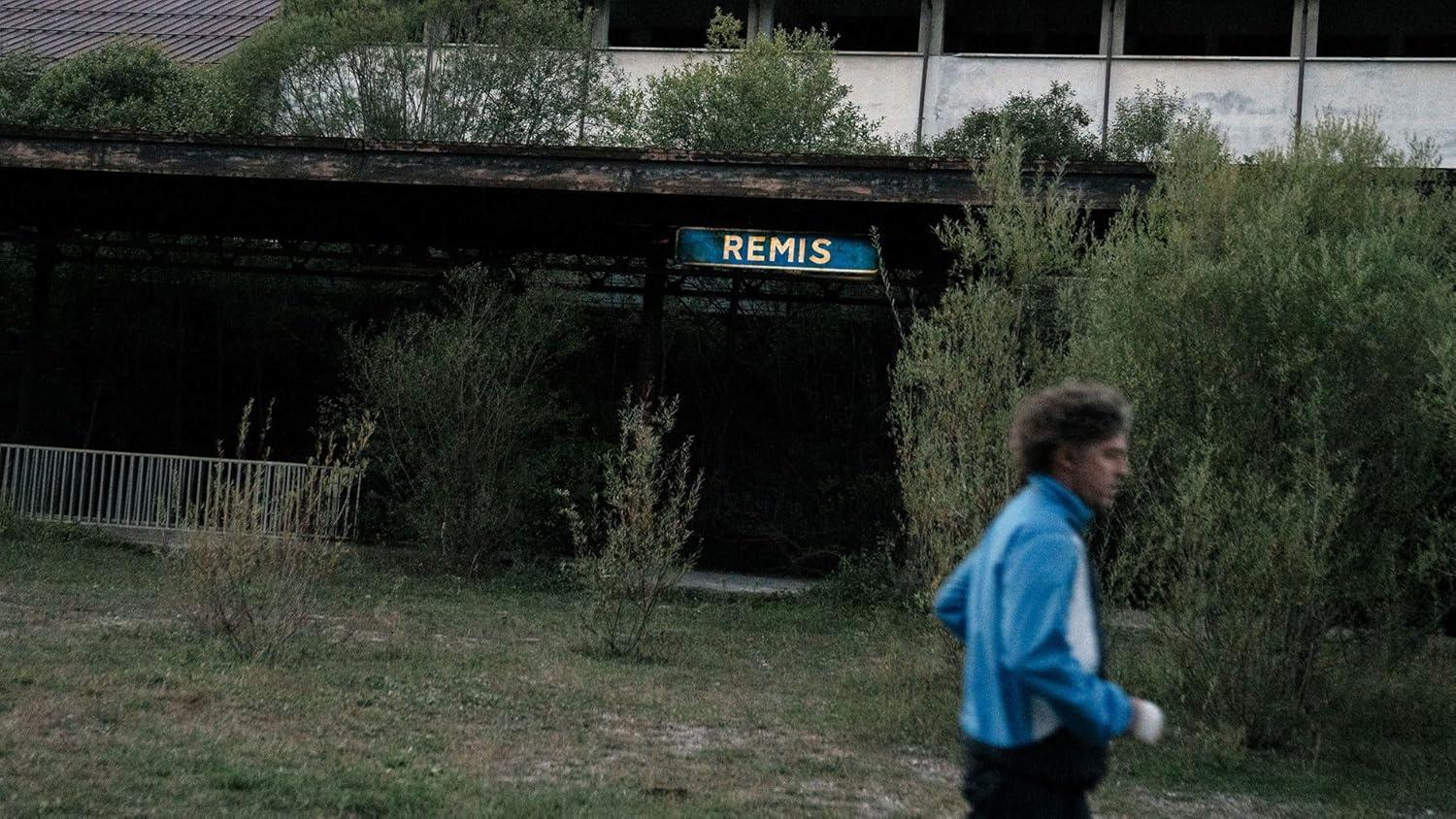 Mann in blauem Trainingsanzug geht an verlassener Bushaltestelle mit Schild REMIS vorbei.